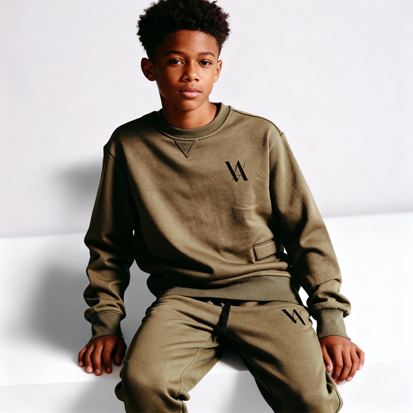 Teenage boy wearing a matching khaki sweatshirt and jogging bottoms with black VA logo.