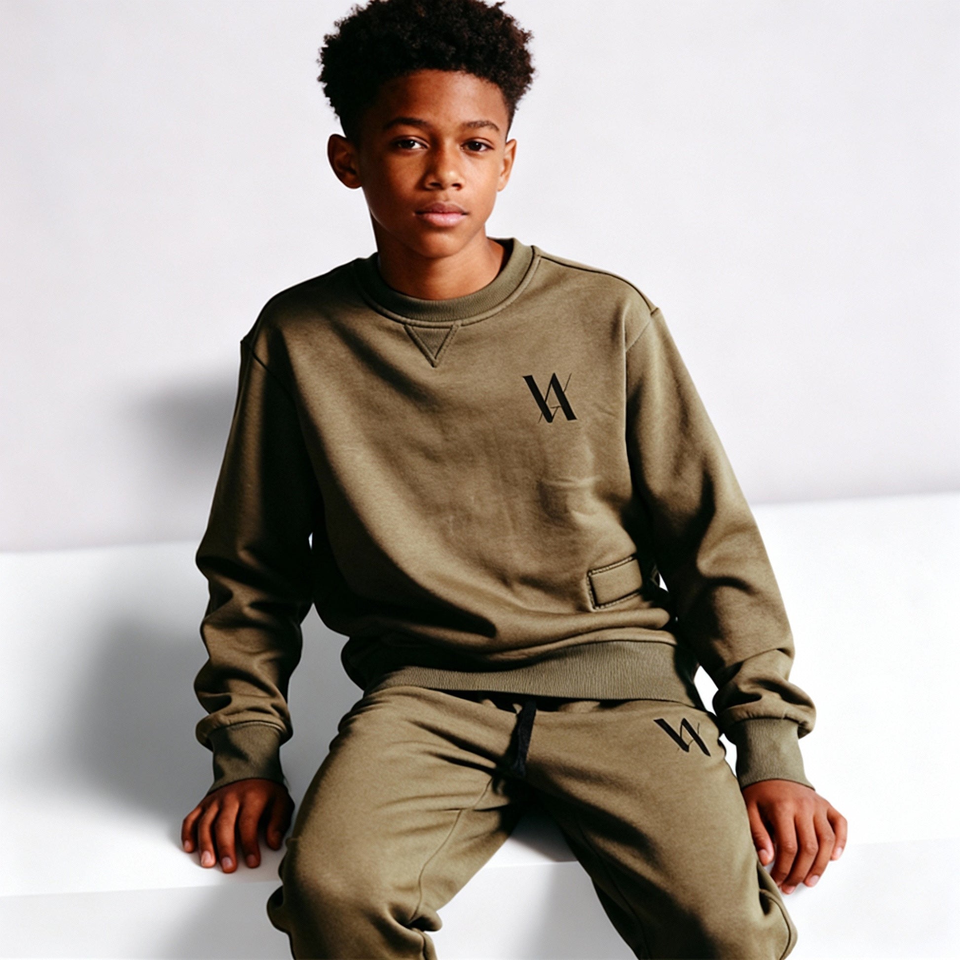 Teenage boy wearing a matching khaki sweatshirt and jogging bottoms with black VA logo.