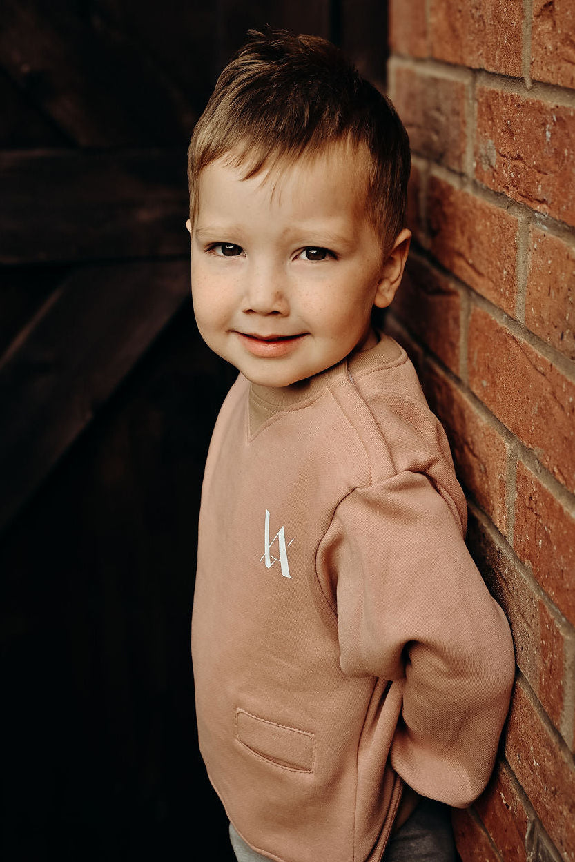 Child wearing a pink sweatshirt with white VA logo leaning against a brick wall